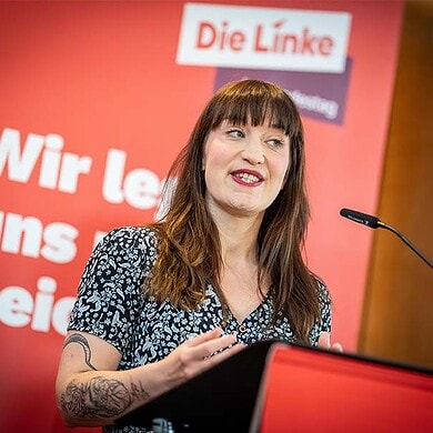 Politikerin bei Wahlkampfrede mit "Die Linke" im Hintergrund.