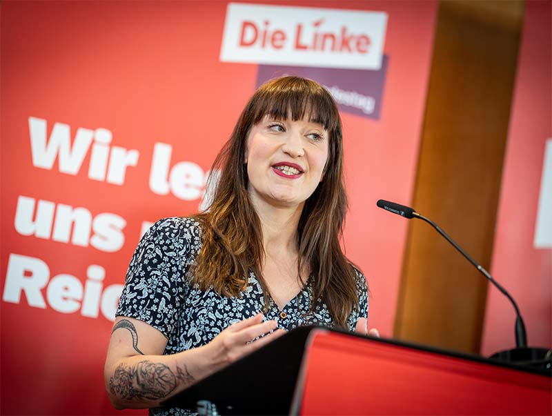Politikerin bei Wahlkampfrede mit "Die Linke" im Hintergrund.